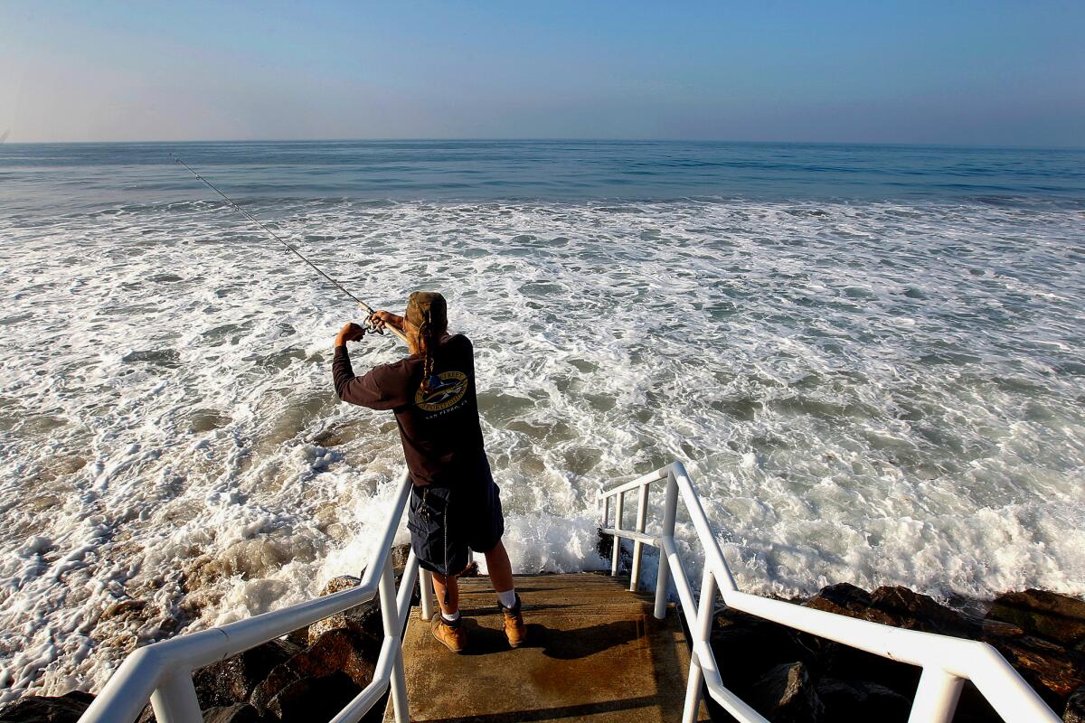 A person stands on a staircase, fishing in the surf below.