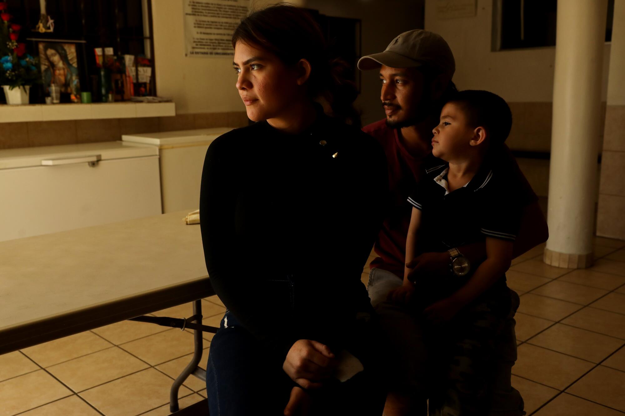 A woman, man and young boy sitting together in a dimly lit room, looking into the distance.