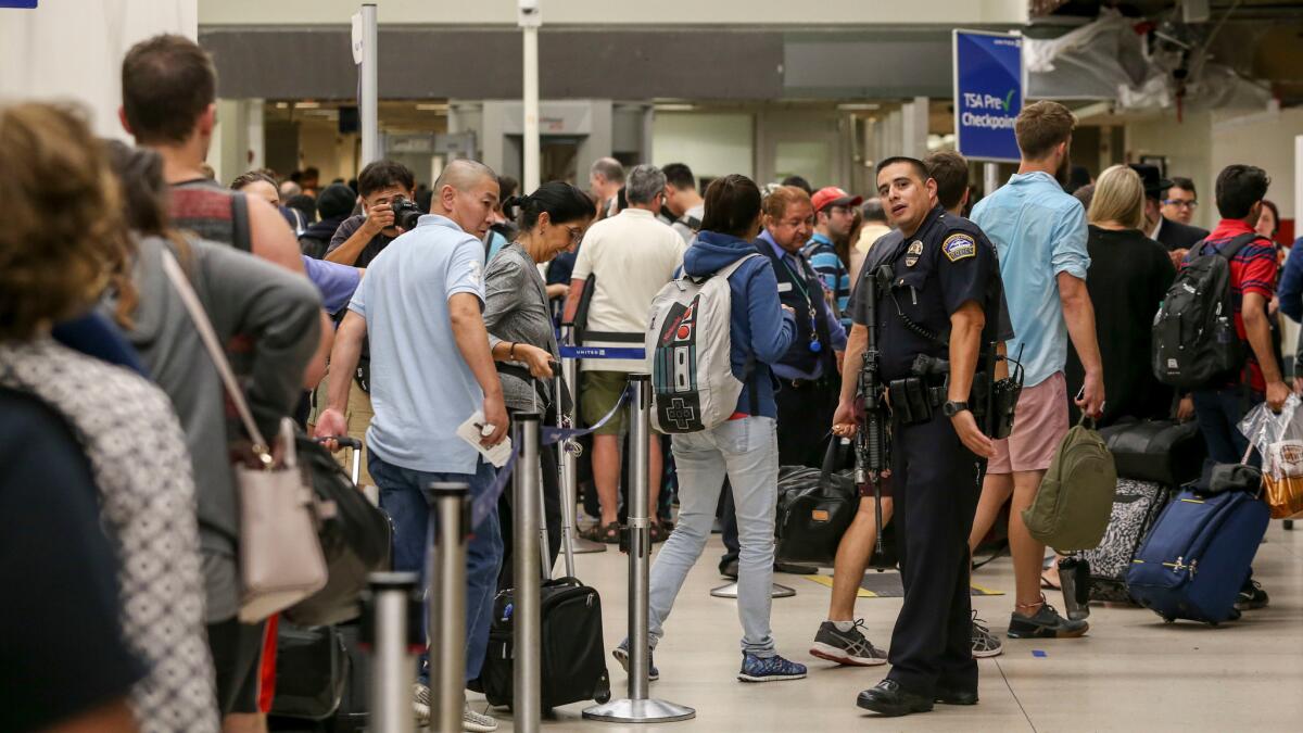 A police officer stands guard while passengers wait in line to be re-screened at Los Angeles International Airport on Aug. 28, after a false report of a gunman opening fire caused people to flee the terminals.