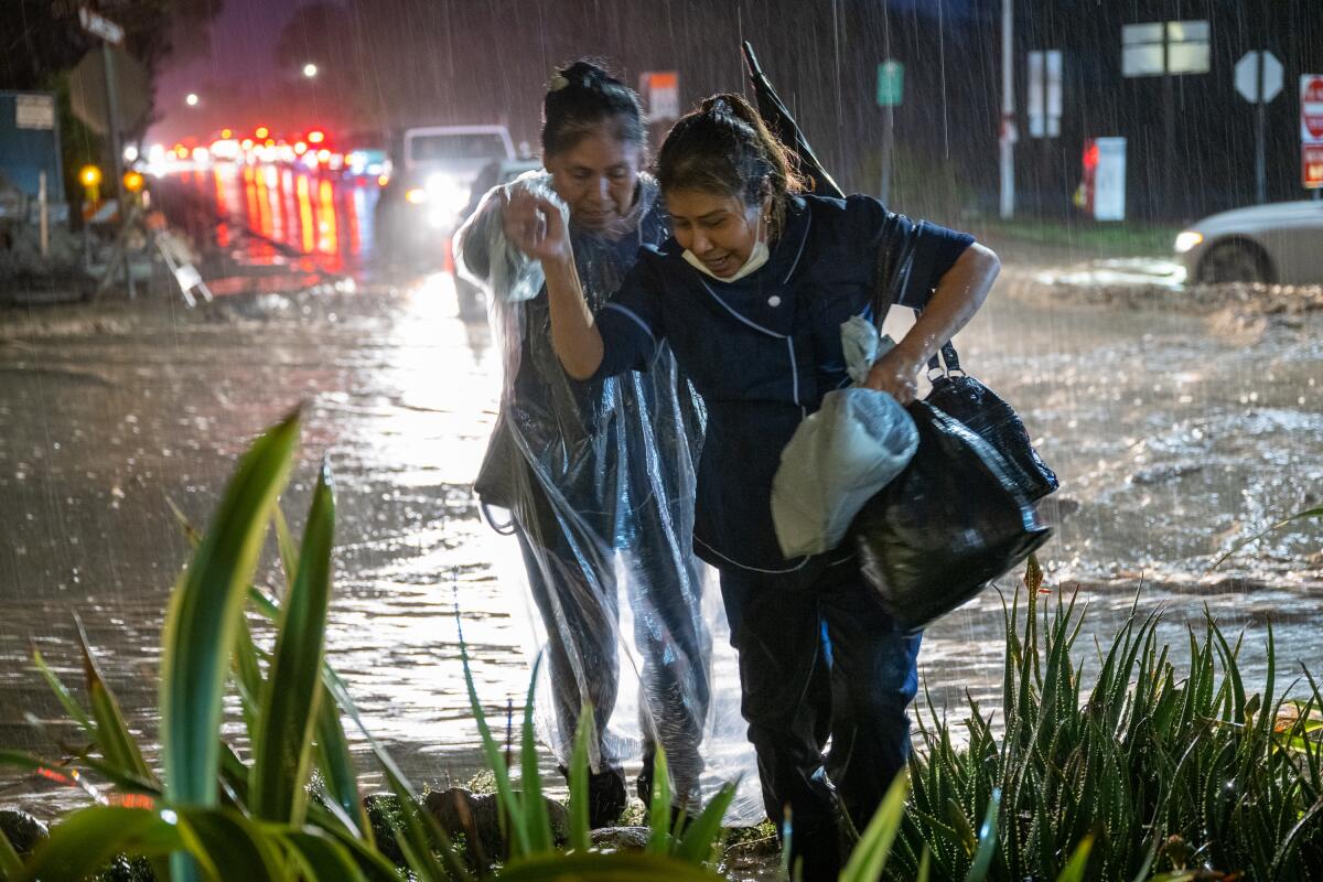 Two women cross a flooded street in pouring rain in Montecito 