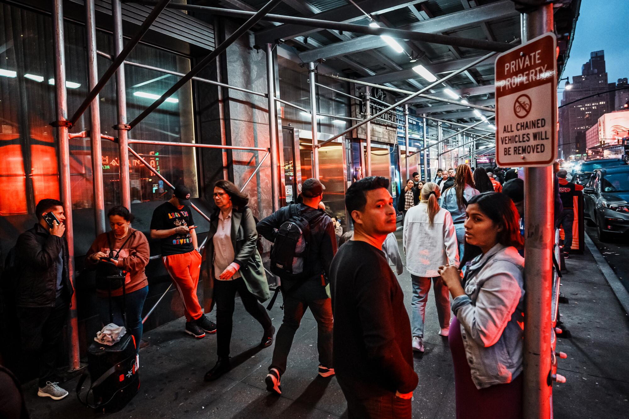 People walk under scaffolding on a city sidewalk.