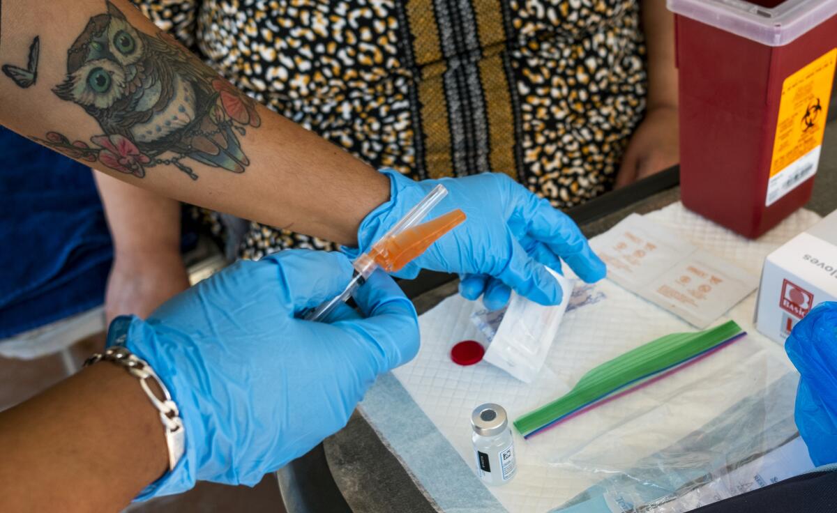 A person wearing blue medical gloves holds a syringe.