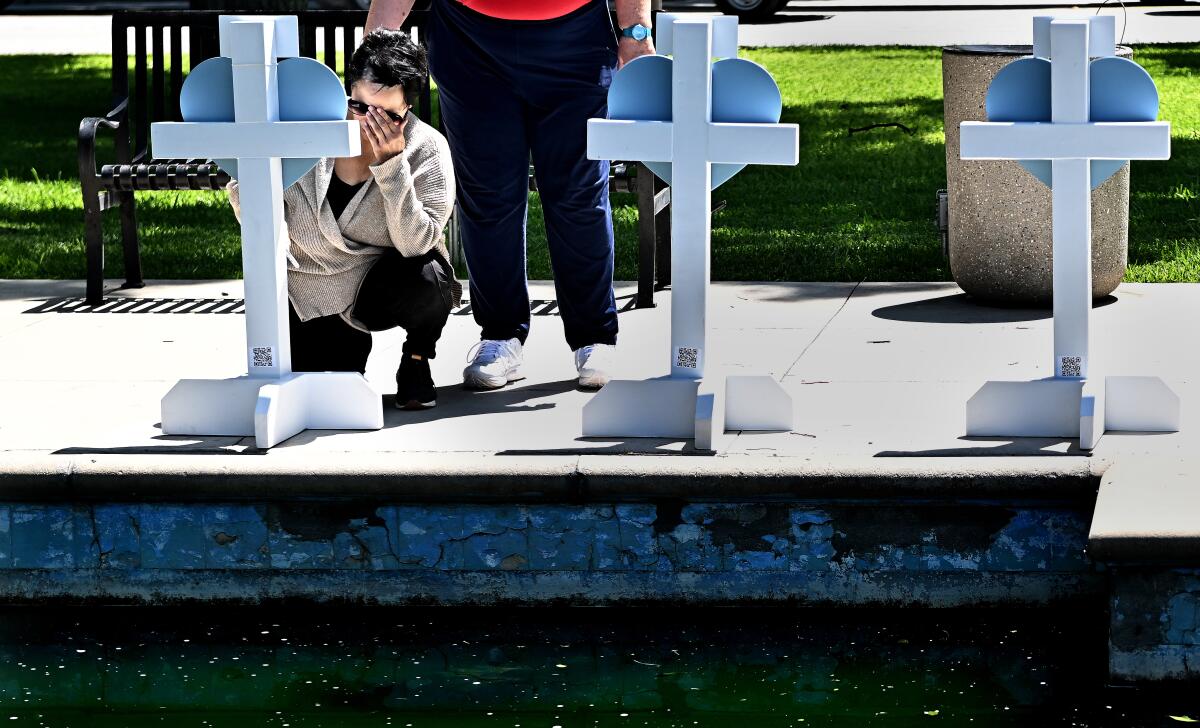 A woman kneels in front of crosses with the names of the children killed at Robb Elementary School in Uvalde, Texas.