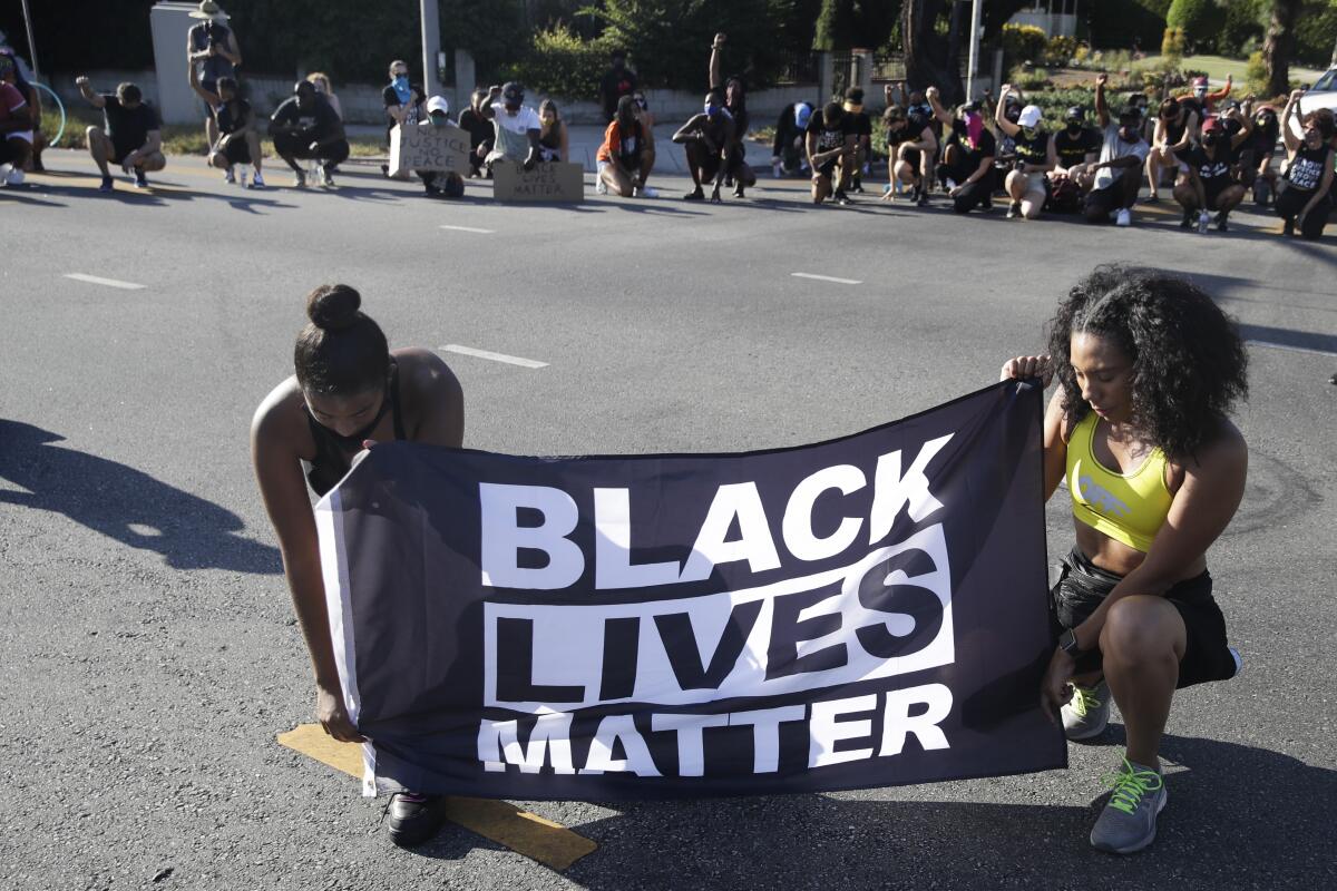 Two women kneel while holding a Black Lives Matter banner during a demonstration.
