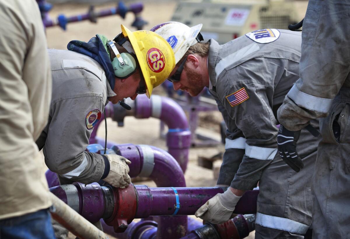 Workers adjust piping during a short pause in water pumping during a natural gas hydraulic fracturing operation outside Rifle, Colo.