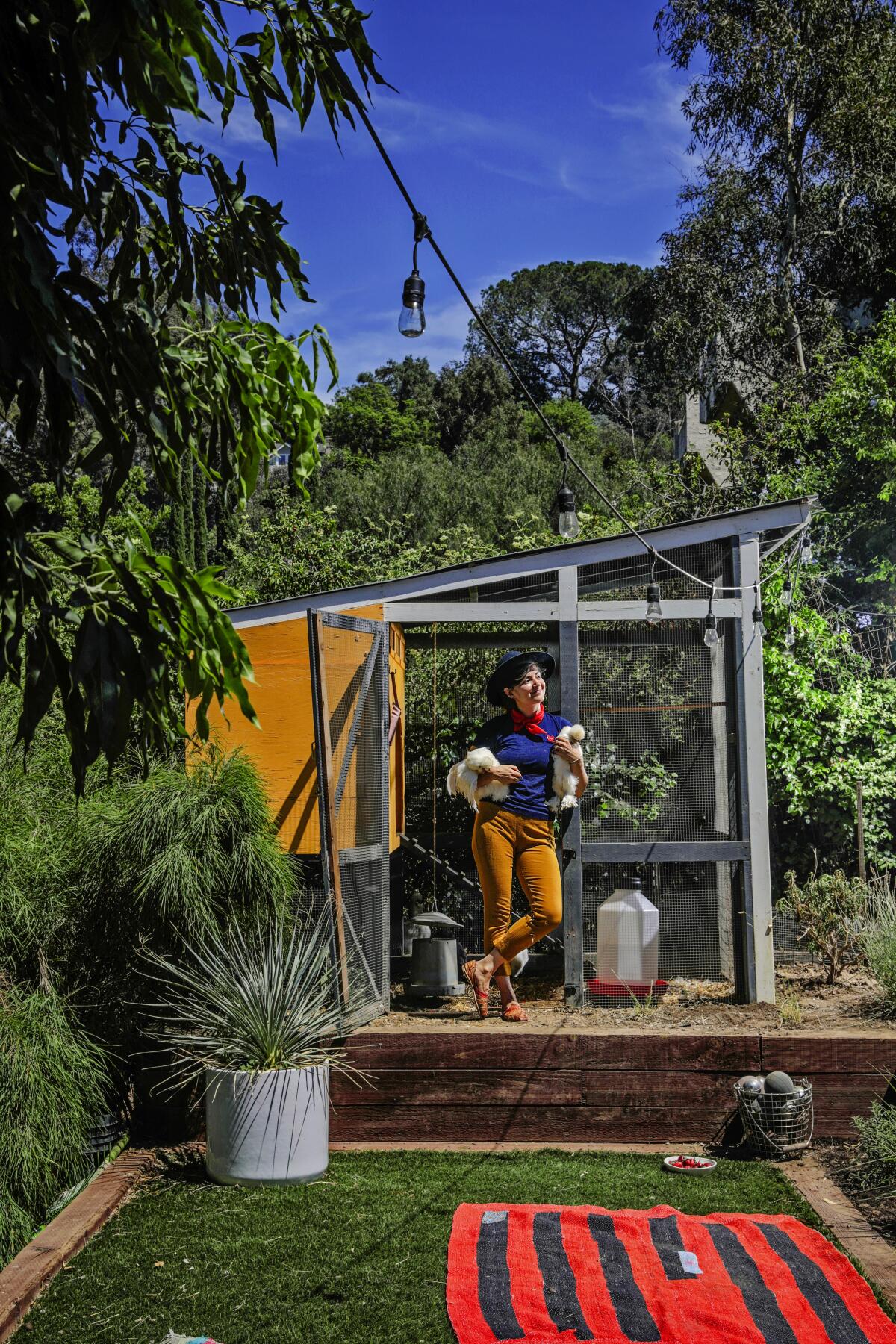 Ellen Bennett stands holding two chickens in their chicken coop.