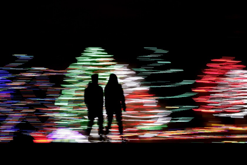 People are silhouetted against a Christmas display, at a park in Lenexa, Kan. 