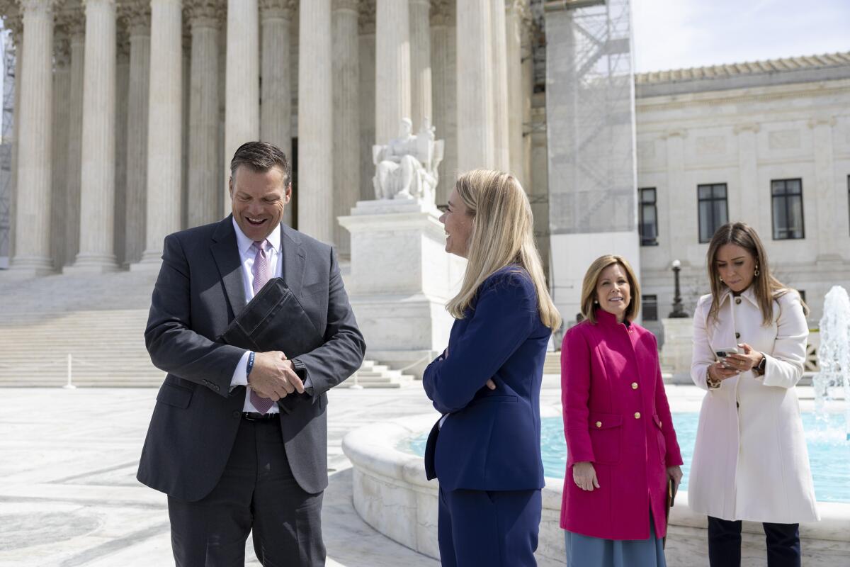 A man and woman speak outside a columned building. 