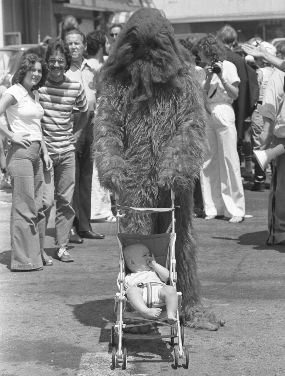 A man in a head-to-toe furry costume pushes an umbrella stroller with a baby in it.