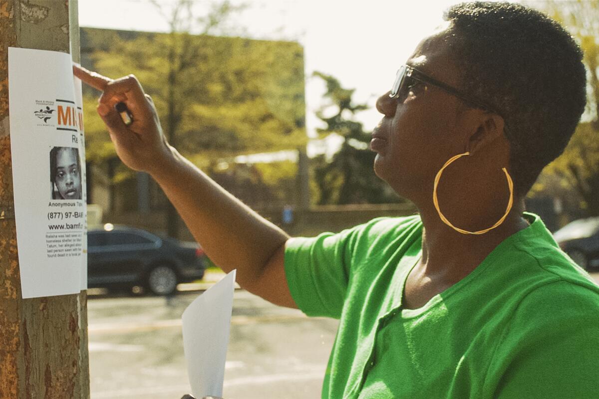 A woman attaches a poster to a utility pole in "Black and Missing" on HBO.