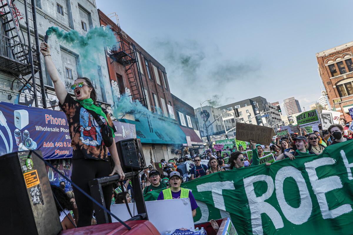 A person stands in the bed of a truck and raises a canister with green smoke as they lead a crowd of marchers.