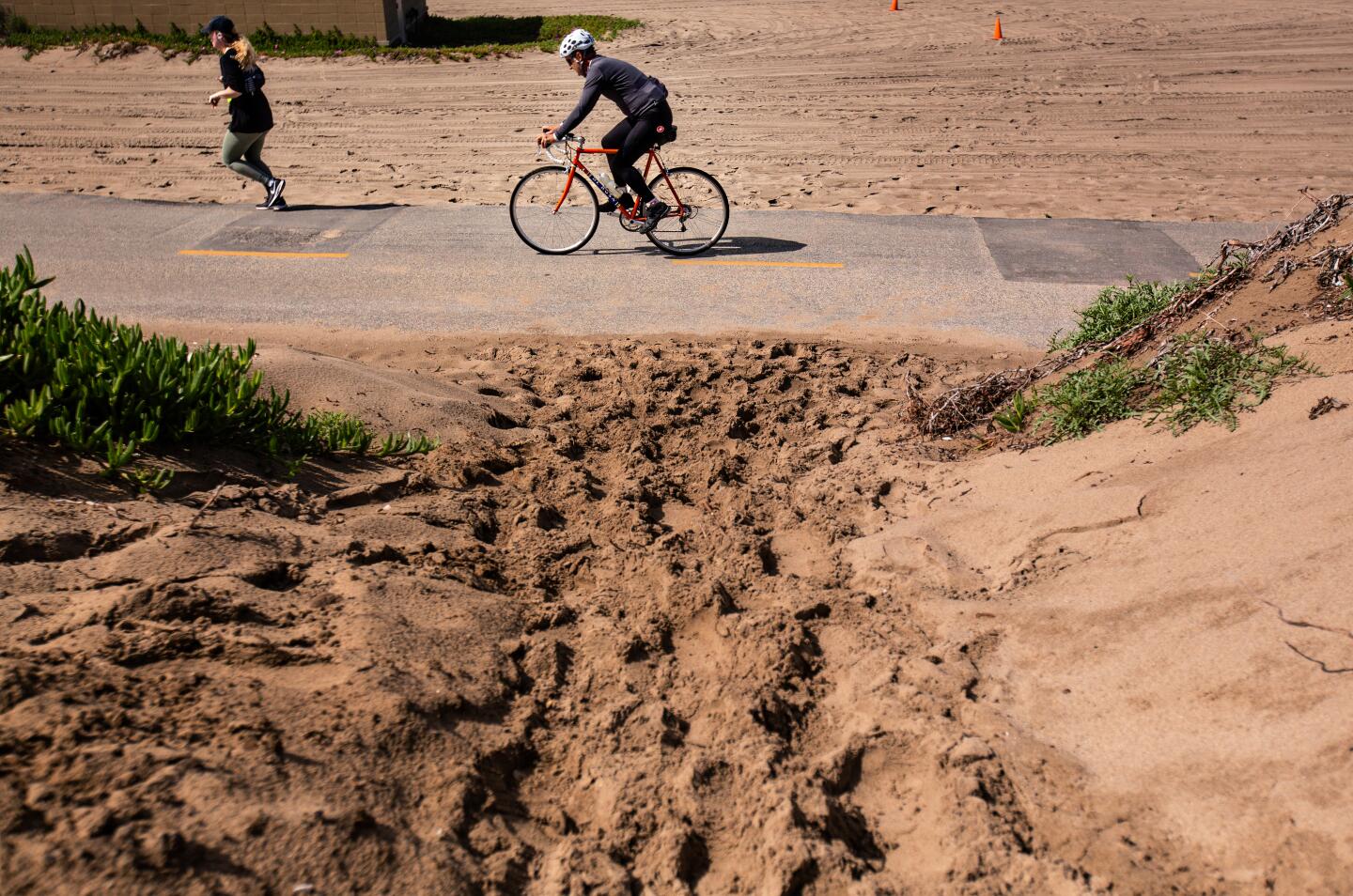 A woman jogs and a man bikes at Dockweiler State Beach on March 15 in Los Angeles. Dockweiler Beach RV Park will temporarily house individuals who may have been ordered to isolate or quarantine by the Department of Public Health due to the novel coronavirus.