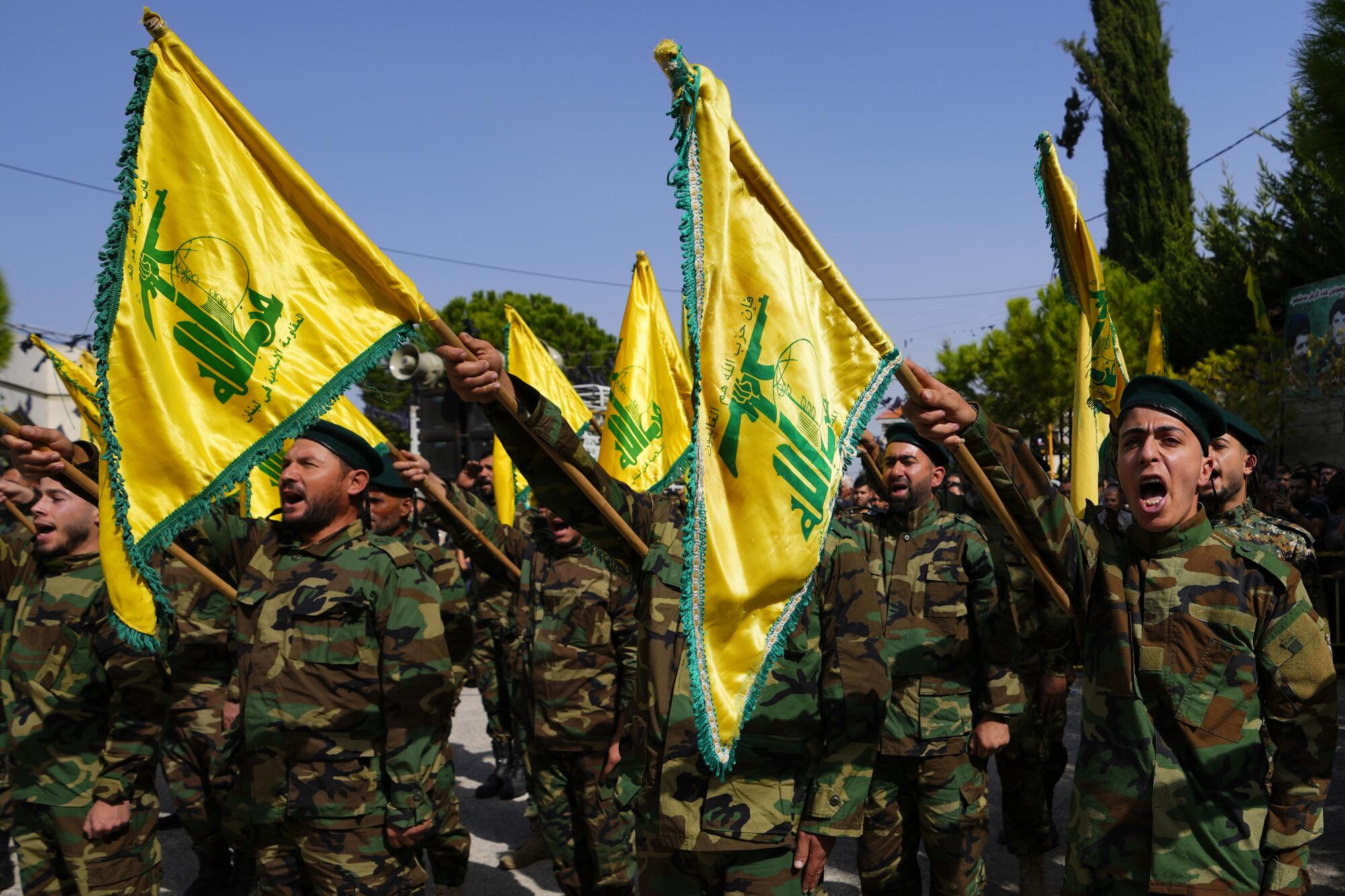 People dressed in military uniforms shout while holding yellow and green flags.