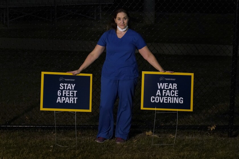 Emergency room nurse L'Erin Ogle poses with coronavirus signs after getting off a 12-hour shift at a nearby hospital where she works Monday, March 8, 2021, in Overland Park, Kan. After a year of working long hours taking care of COVID-19 patients, Ogle feels obligated to speak out when she sees misinformation related to the pandemic in her community. (AP Photo/Charlie Riedel)