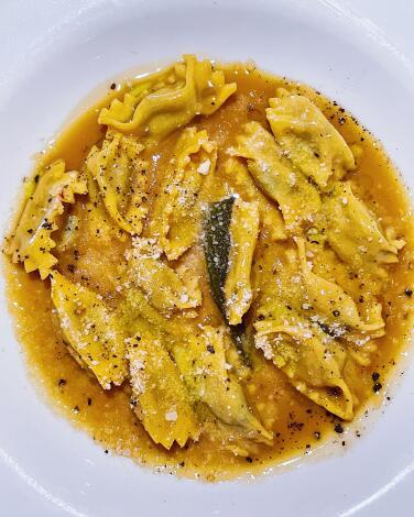 Plin dell’ Alta Langa: small pinched, stuffed pasta in a golden sauce on white plate