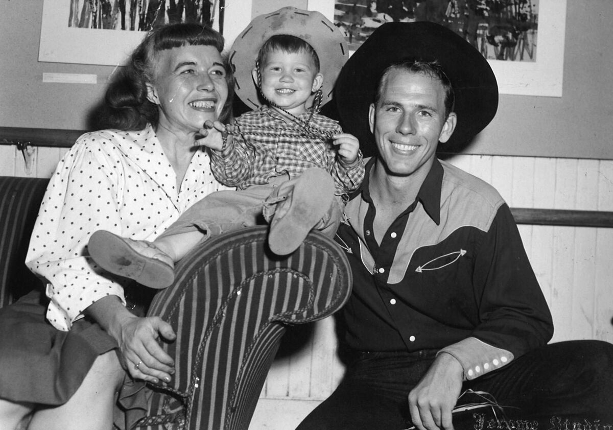 A black-and-white photo of a toddler in between a woman, left, and a man