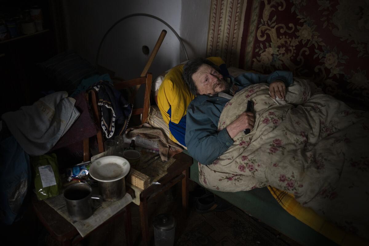 An old man rests in bed in his partially destroyed home, which was hit by Russian shelling.