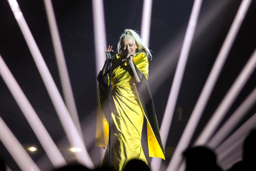 A blond woman in a yellow dress singing into a microphone