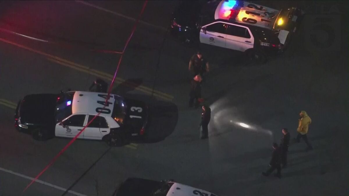 Aerial view of officers standing next to police cruisers and red crime scene tape on a street