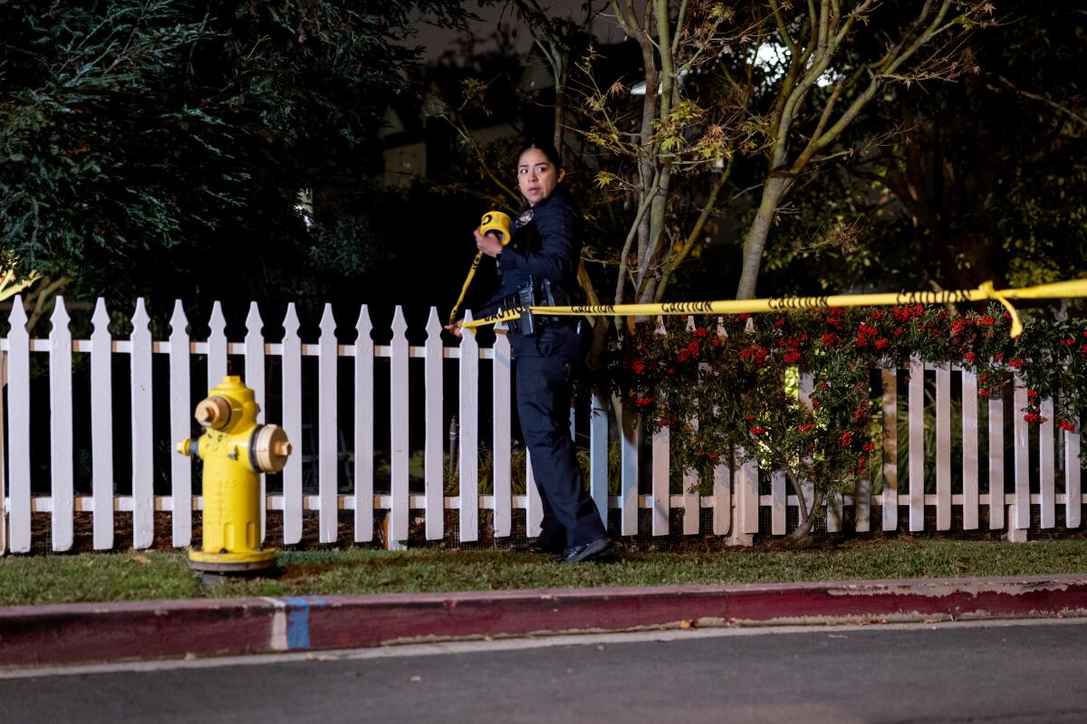 An officer stretches yellow crime-scene tape near a white picket fence.
