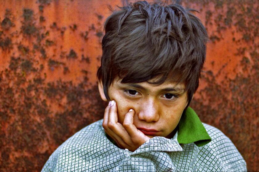 Denis Contreras, 12, awakens after sleeping in a gravel-filled hopper car in a Tapachula, Mexico, rail yard in August 2000. His mattress was crumpled paper, his blanket an oversize pullover.