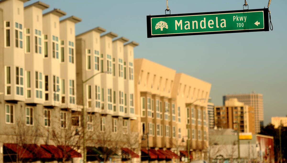 A street sign for Mandela Parkway is in sharp focus, with the Mandela Gateway apartments in Oakland in the background.