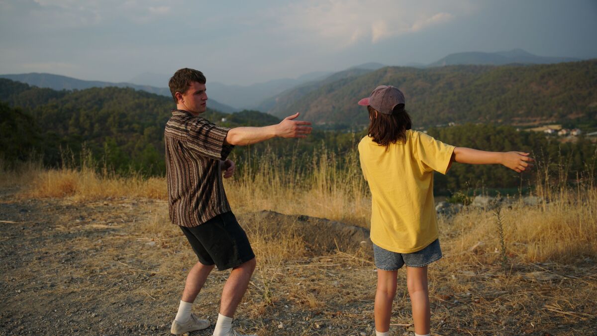 A guy and a girl are dancing in a field with low mountains in the background