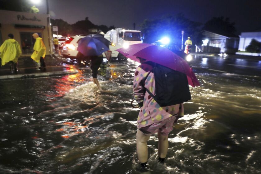 People cross a flooded street in Auckland, Friday, Jan. 27, 2023. Record levels of rainfall pounded New Zealand's largest city, causing widespread disruption. (Dean Purcell/New Zealand Herald via AP)