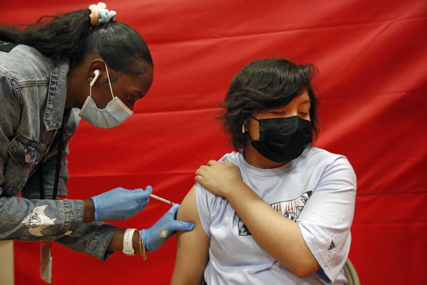 LOS ANGELES, CA - MAY 17: Alex Olvera, 15, is vaccinated with Pfizer by Rickeyva Foster, left, at the Manual Arts High School basketball and gym building in downtown on Monday, May 17, 2021 in Los Angeles, CA. The school is one of 200 sites that the Los Angeles Unified School District has deployed mobile vaccination teams to get as many shots into students' arms as possible. (Dania Maxwell / Los Angeles Times)