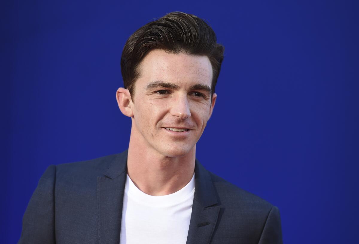 With a blue backdrop behind him, Drake Bell smiles.