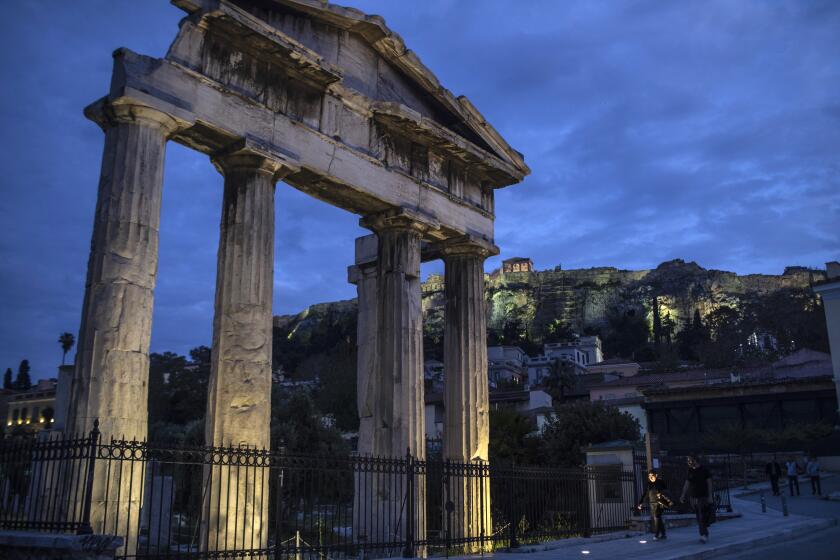 People walk in front of the Gate of the ancient Roman agora with the ancient Acropolis hill seen in the background in the traditional Plaka district of Athens, as lockdown measures continue to prevent the spread of the coronavirus, on Monday April 27, 2020. (AP Photo/Petros Giannakouris)