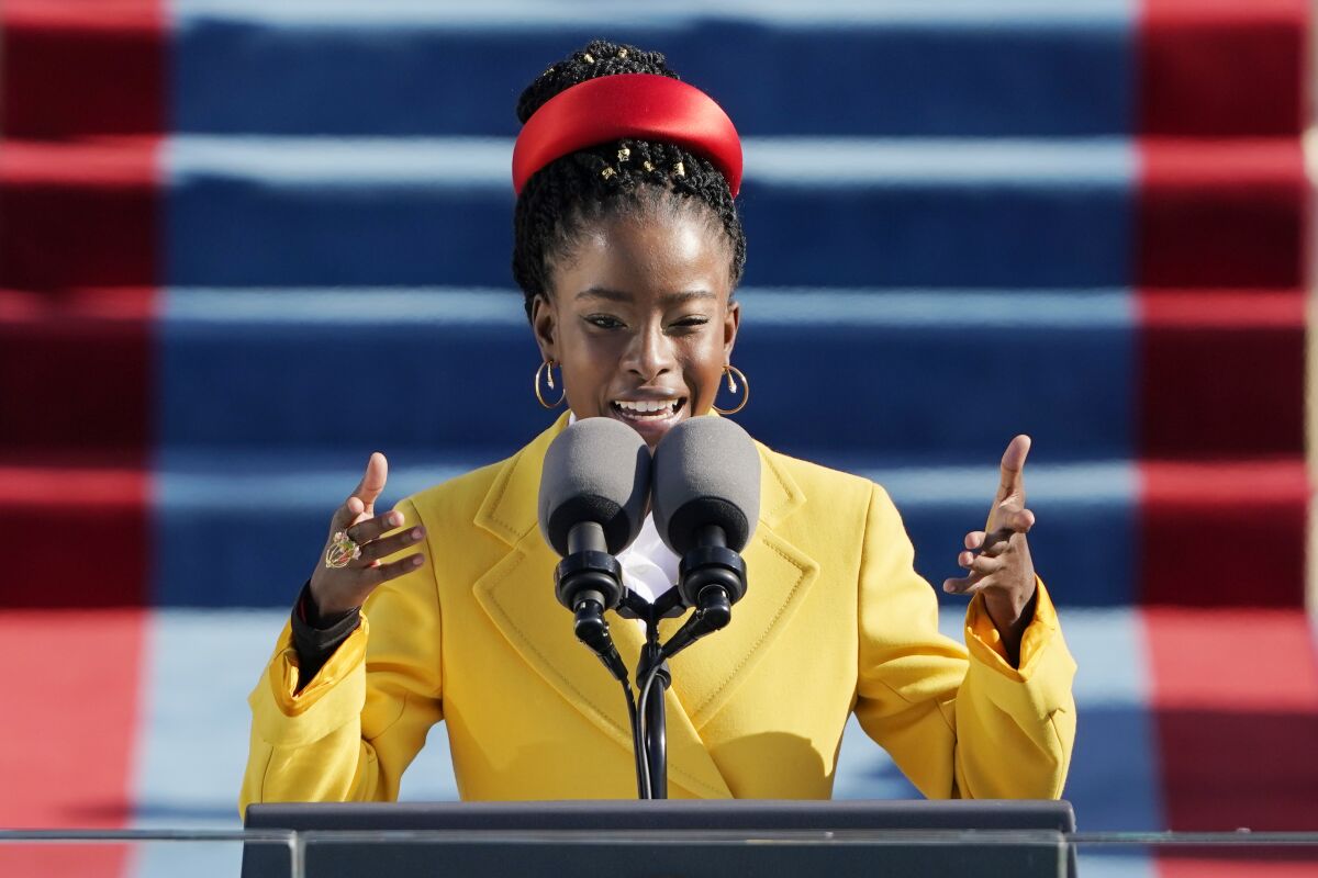 A woman in a yellow coat and red headband speaks at a microphone.