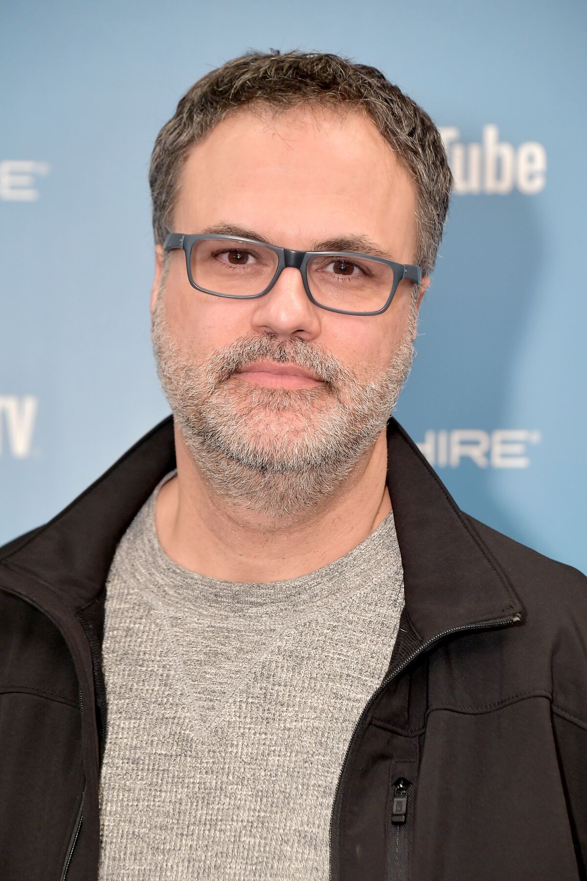 A headshot of a man in glasses and a gray t-shirt