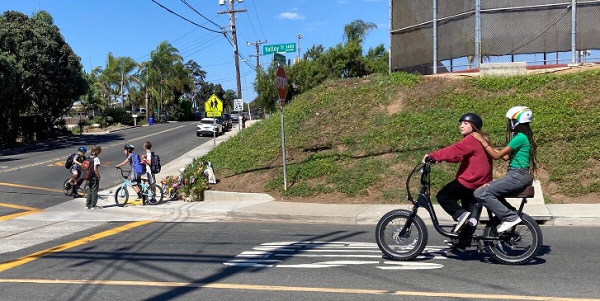 Two riders on an e-bike approach the corner of Valley Street and Basswood Avenue in Carlsbad.