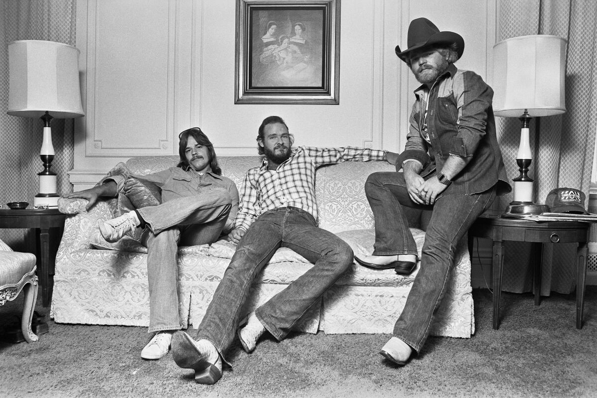 A black-and-white photo of three men, the one on the right wearing a cowboy hat sitting on a couch.