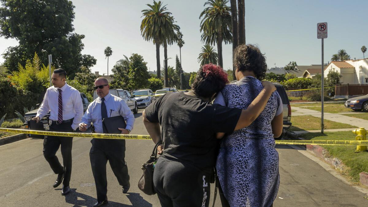 A woman comforts the wife of a man who died in a shooting that left four dead and 12 others wounded at a home on 2900 block of South Rimpau Boulevard in West Adams.