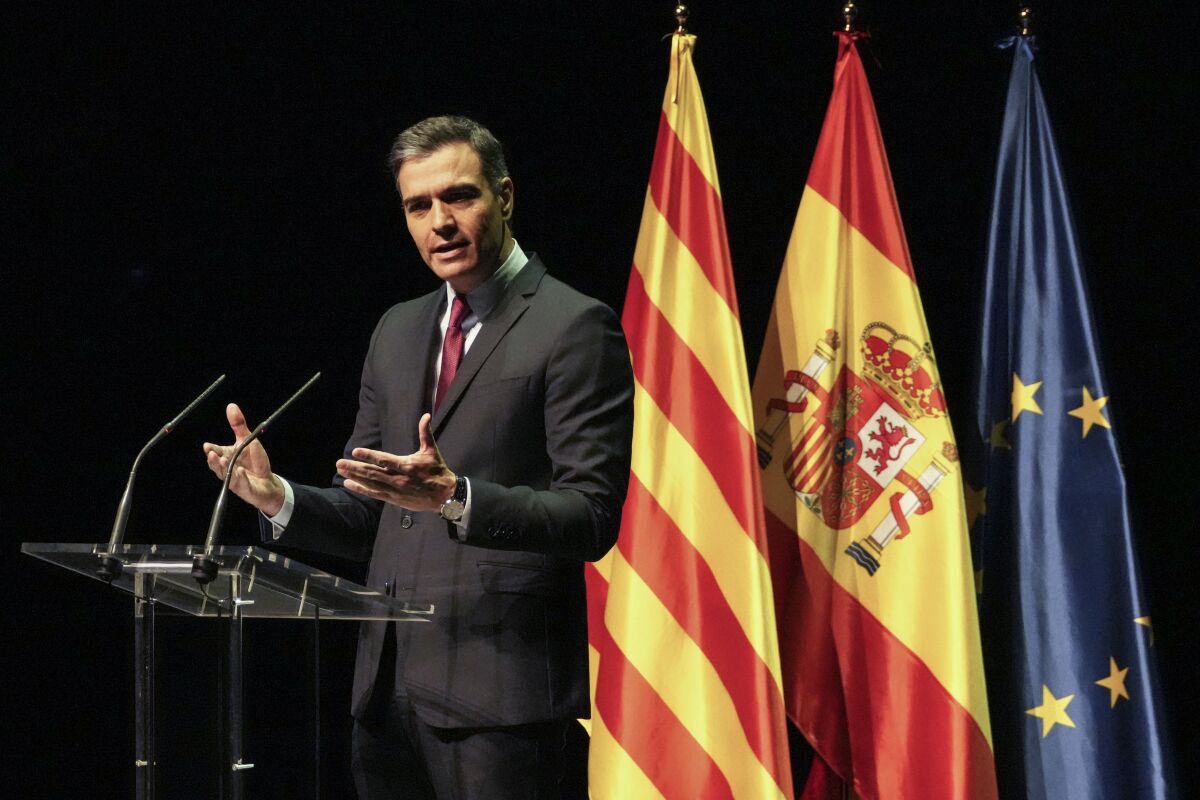 Spanish Prime Minister Pedro Sanchez stands at a lectern near three flags