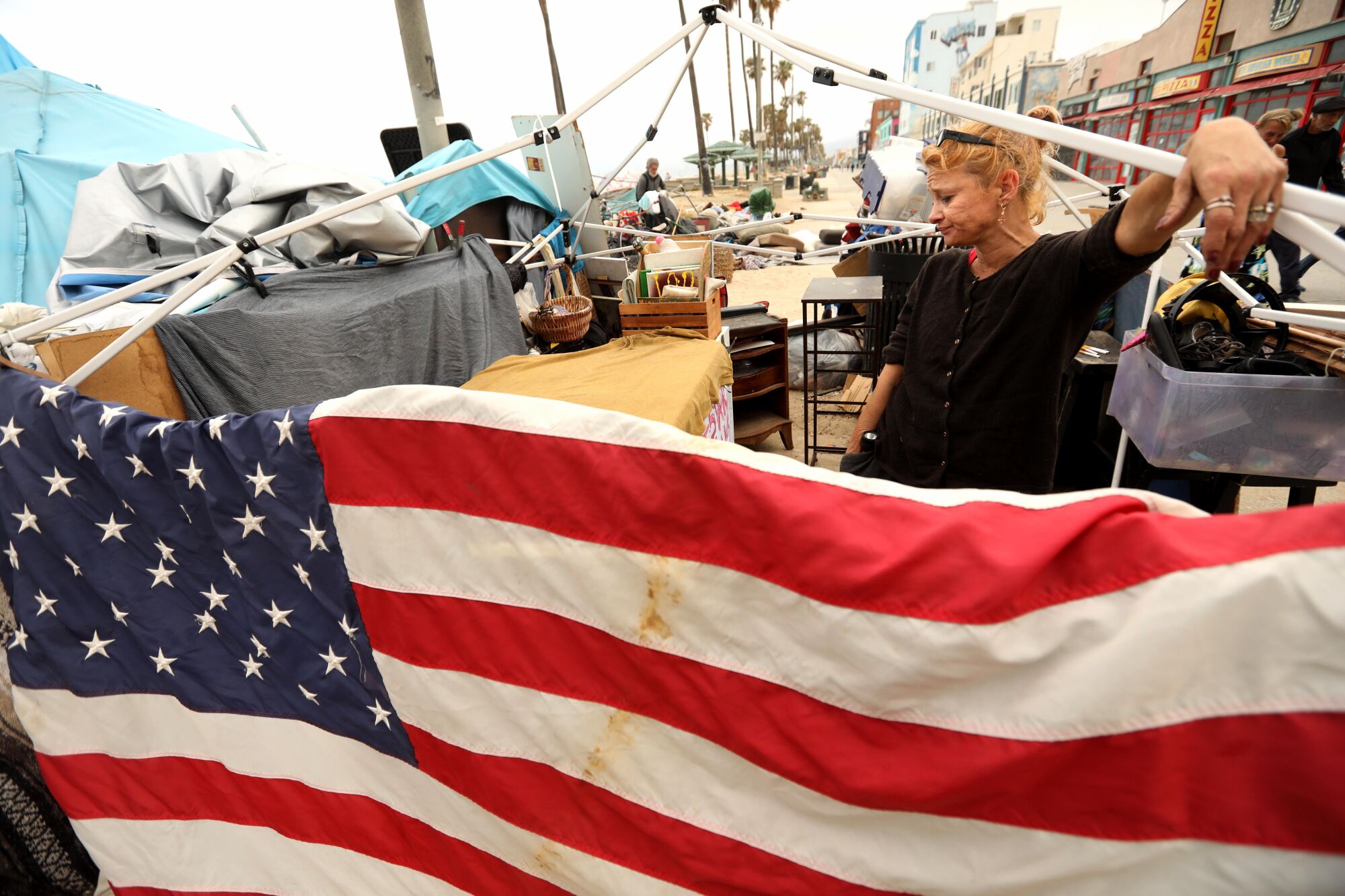 A woman stands in a homeless camp with an American flag in the front