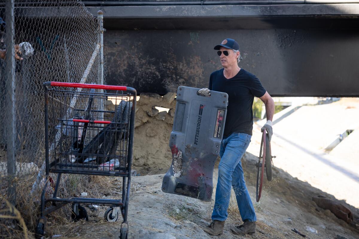 A man carries a large rectangular object past an abandoned shopping cart.