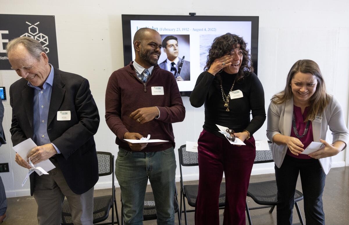 Four people wearing name tags smile and laugh in disbelief, standing in front of a portrait of late donor Jay Kahn.