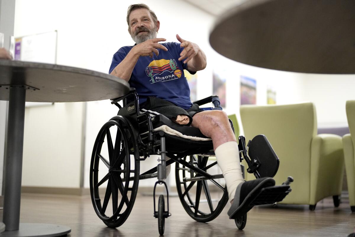 A bearded man with one leg, seated in a wheelchair, gestures with his hands while speaking 