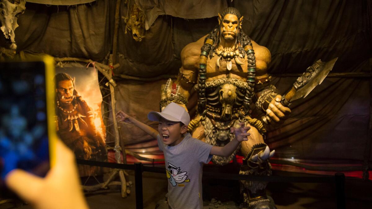 A child poses in Beijing front of a statue of a character from the movie "Warcraft" on Friday. The movie has a strong fan base in China.
