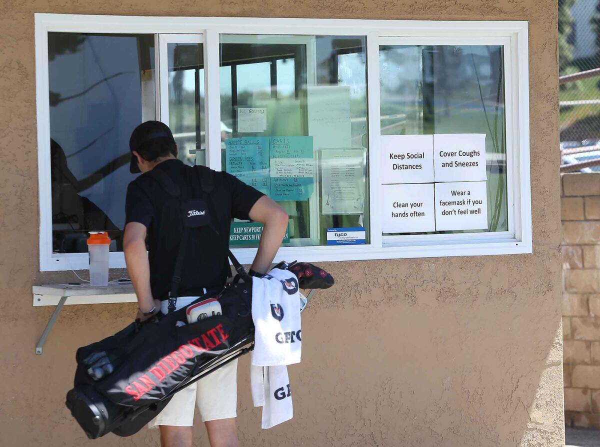 Quentin Hill, a golfer at San Diego State University, orders a bucket of golf balls for practice on the range as messages of safety protocols are placed in the window at the Newport Beach Golf Course on Friday.