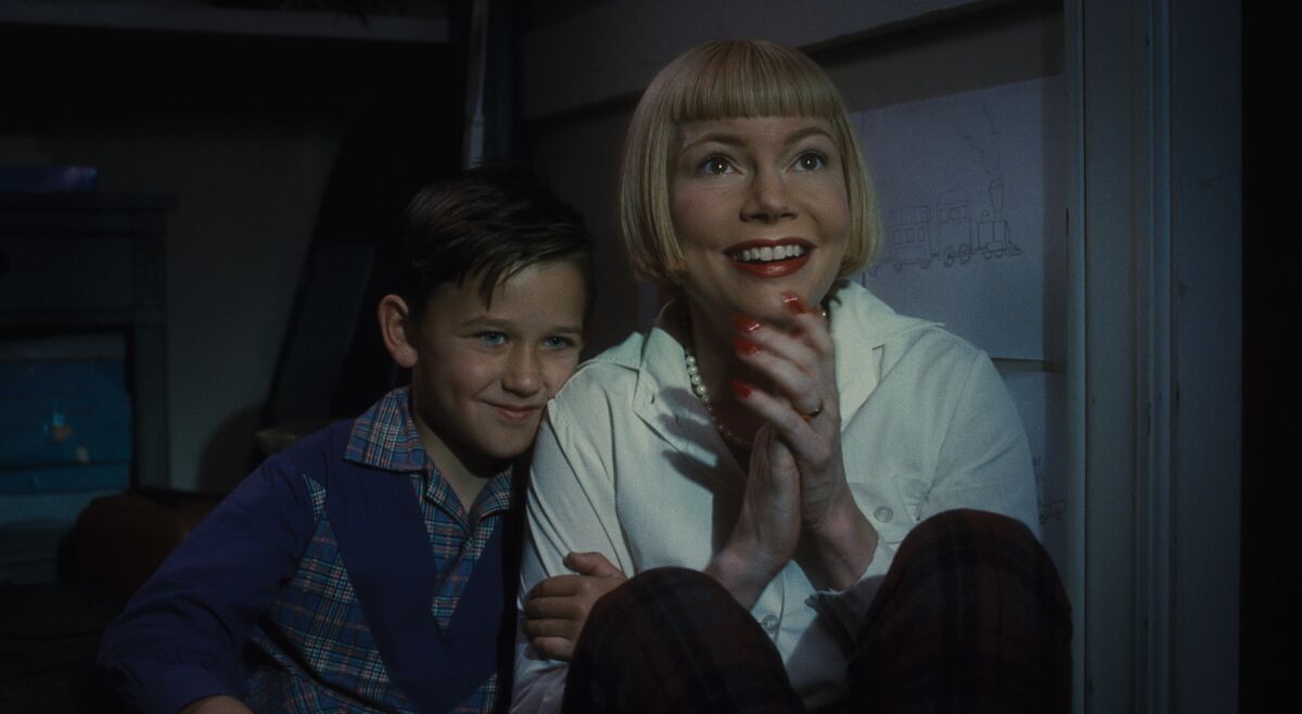 A woman sits close with her young son, both smiling in a scene from "The Fabelmans."