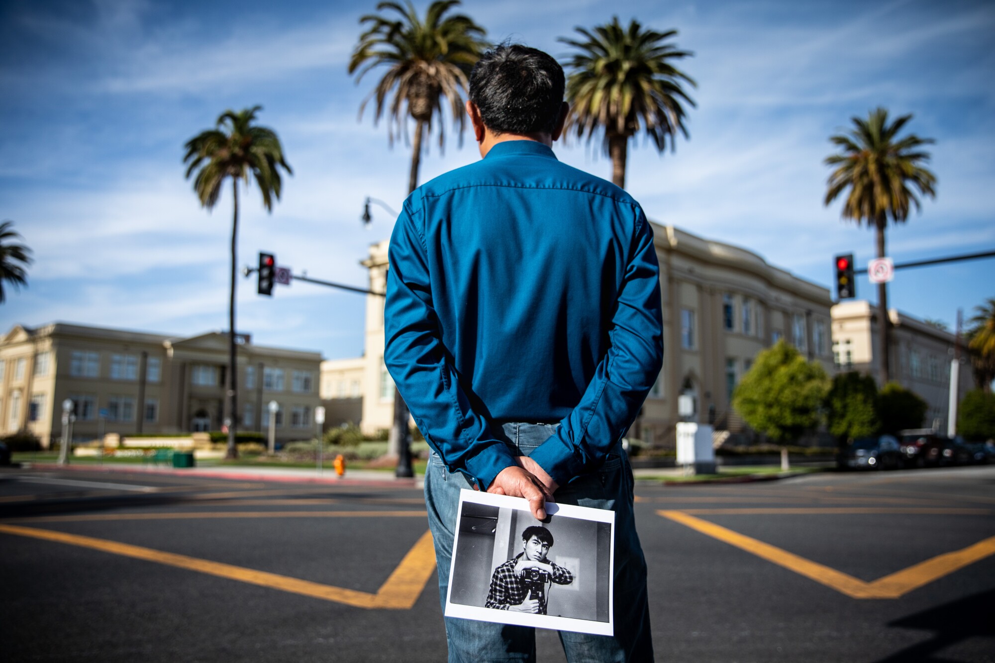 A man stands facing a crosswalk holding a photograph.
