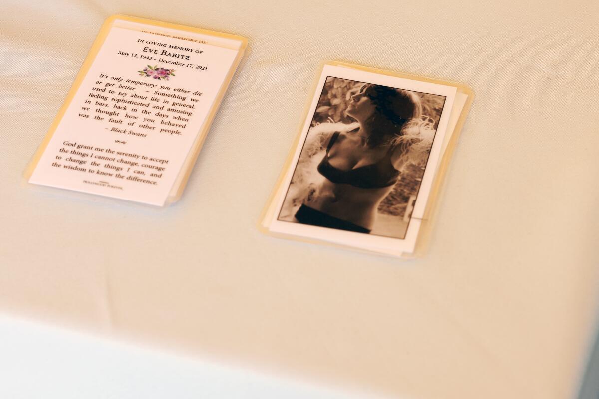 Memorial cards with a prayer and an image of Eve Babitz in a bra and underwear sit on a table. 