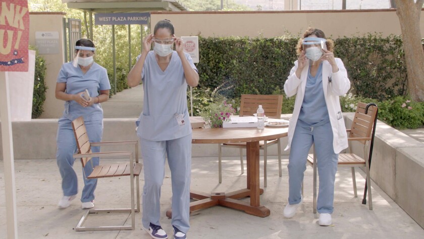 Three people in an outdoor area wearing scrubs, face shields and masks.