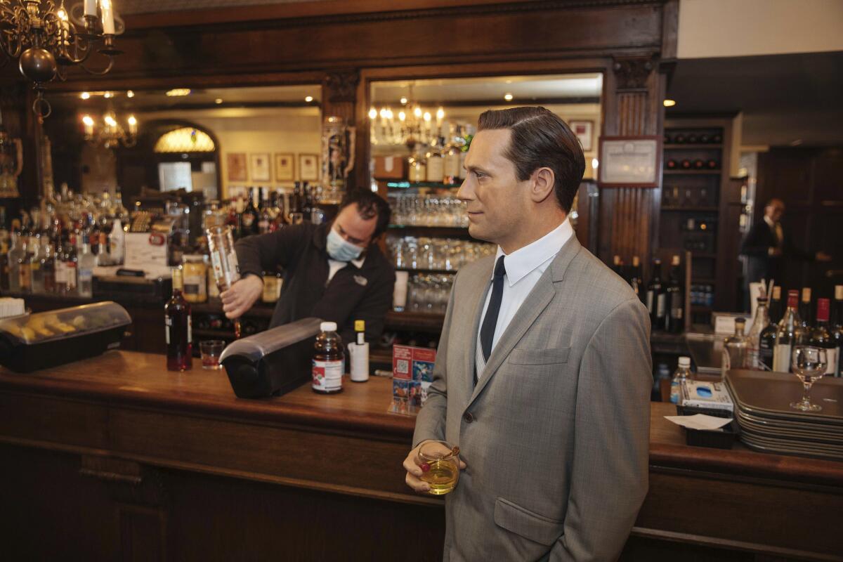 A wax statue of actor Jon Hamm stands by a bar