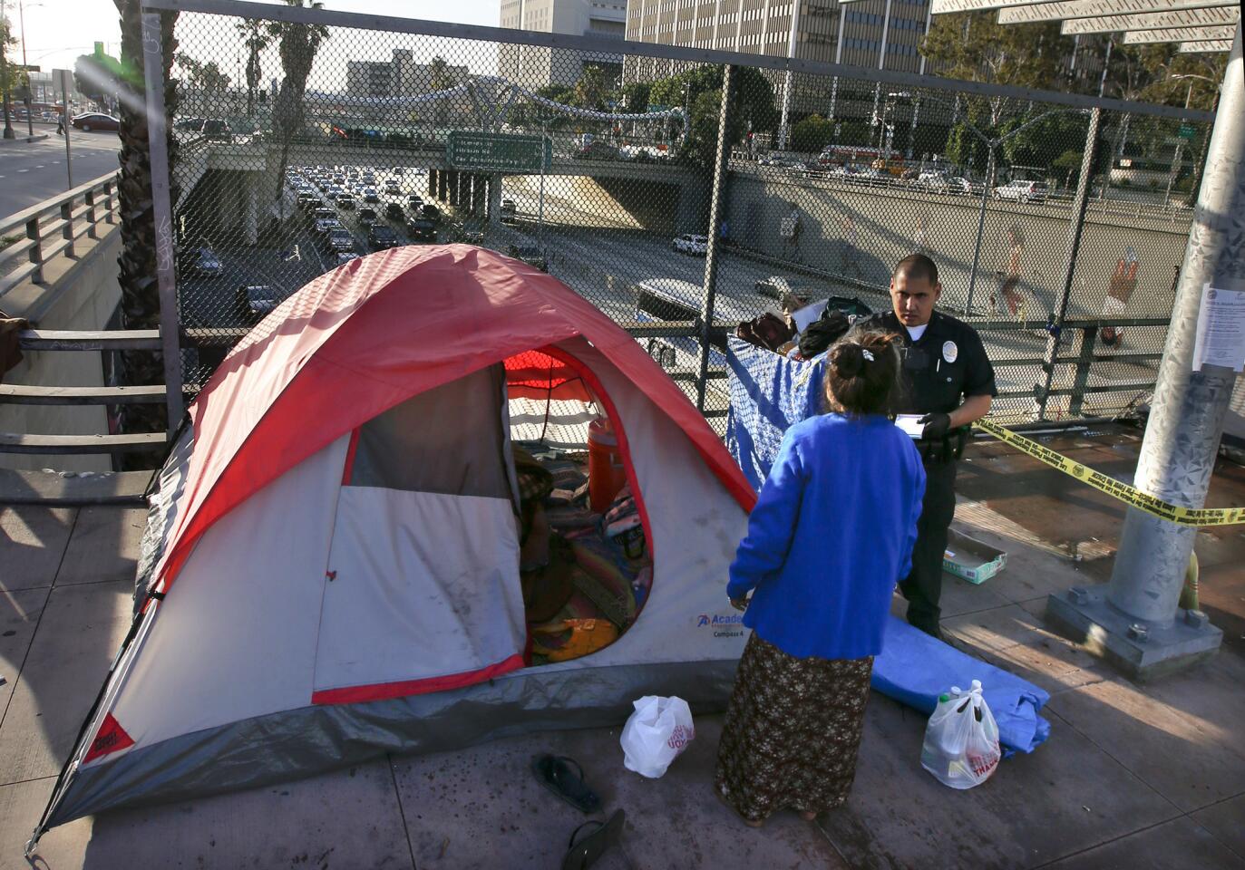 An LAPD officer makes contact with Ry Thounry, 50, while she tries to clean up her tent on the Main Street overpass above the 101 Freeway in downtown L.A.