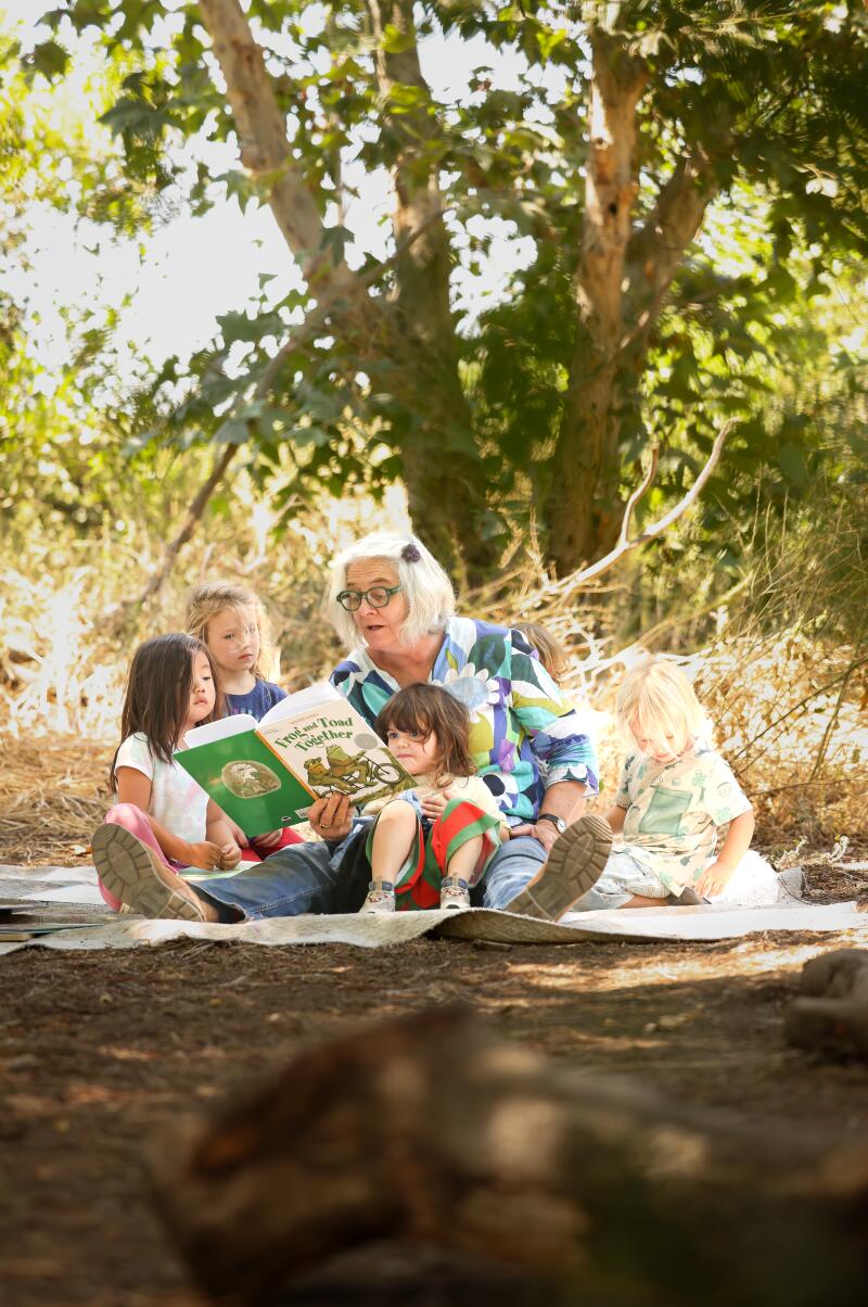 A woman reads to children outside.